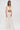 A woman stands against a white background wearing high-waisted wide-leg pants and the PEARL HEAVEN BEADED TOP, which features padded shoulders and a dramatic overlay of opulent pearl beads draping from her shoulders and arms.