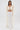 A woman with straight brown hair and a serious expression stands against a white background, wearing pleated wide-leg pants and the PEARL HEAVEN BEADED TOP, which has padded shoulders and dramatic cape-like pearl beading.