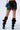 A person is wearing black high-heeled shoes with ruffled thigh-high boots, a stretchy faux leather LATE NIGHT VIBES MINI SKIRT featuring geometric diamonds, and has a green handbag on their shoulder. The image only shows from the waist down, highlighting the edgy and fashionable outfit.