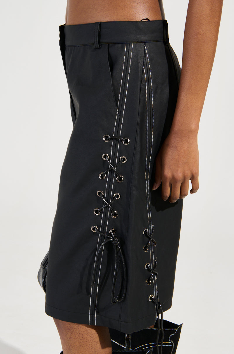 Wearing the chic high-rise COLD HEART SHORT with white contrast stitching and lace-up sides, a person stands with their hand by their side. The black faux leather shorts are styled with black footwear against a neutral background.