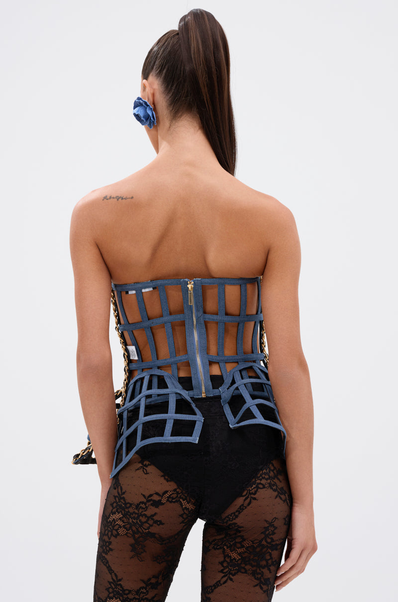 A woman with a high ponytail is seen from behind wearing the DOWN SOUTH CHAIN DETAIL BUSTIER TOP in a blue grid pattern, paired with black lace shorts and a blue flower hair accessory. Her back is exposed, revealing a small shoulder tattoo. 5