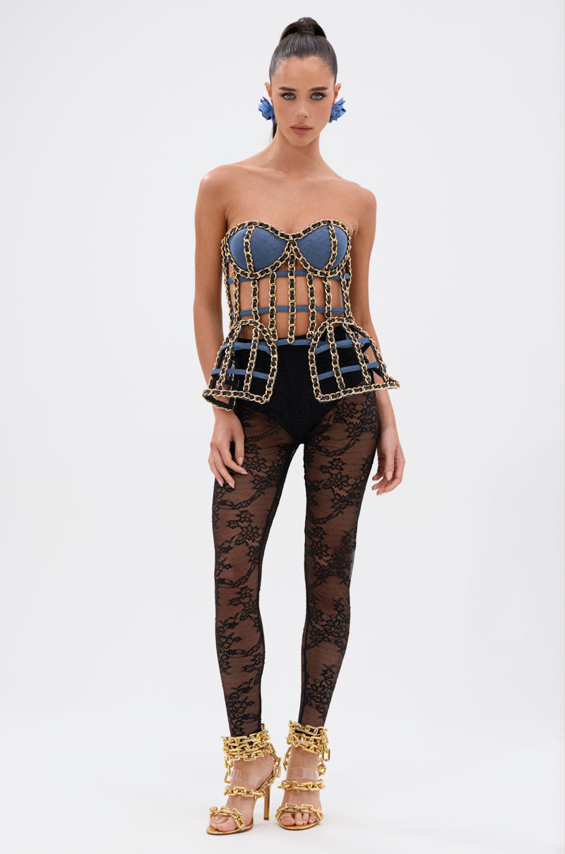 A woman stands against a plain background wearing the DOWN SOUTH CHAIN DETAIL BUSTIER TOP, high-waisted black shorts, black lace tights, gold chain sandals, and blue hair accessories. 6