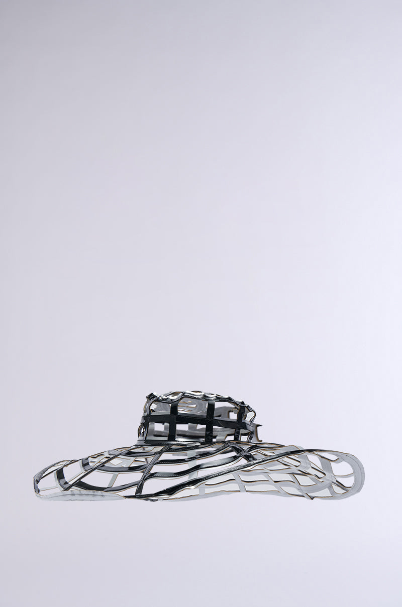 The IM OFF THE GRID BLACK SILVER HAT is a metallic, abstract headpiece with an intricate lattice structure. It showcases a black silver color, featuring an oversized brim and a distinct top section. This design merges futuristic aesthetics with a touch of faux leather against a plain gray background.
