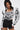 A woman models the FRIEDA PUFF LONG SLEEVE CROPPED BLOUSE, showcasing bold black abstract swirls, 3D piping details, and a metallic back zipper, paired with high-waisted black shorts.