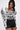 A woman with long dark hair wears the FRIEDA PUFF LONG SLEEVE CROPPED BLOUSE, featuring bold black abstract patterns and 3D piping, paired with high-waisted black shorts against a plain background.