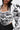 A woman with long, wavy dark hair models the FRIEDA PUFF LONG SLEEVE CROPPED BLOUSE, featuring bold black abstract piping and puffed sleeves, against a plain white background.