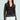 Someone with long hair is wearing a chic SEDUCTION & BEAUTY STRUCTURED BLOUSE, featuring sheer long sleeves over a black top. Paired with high-waisted white pants with buttons, they complete the Y2K-inspired look by holding a small black accessory.