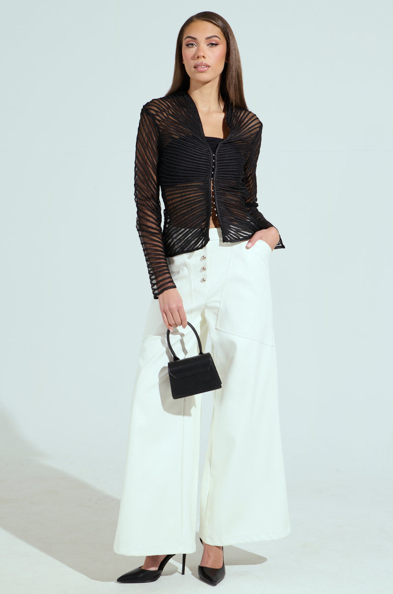 Wearing the SEDUCTION & BEAUTY STRUCTURED BLOUSE paired with white wide-legged pants, a person stands against a plain background, exuding a chic Y2K-inspired style. They hold a small black handbag, wear black pointed heels and have one hand stylishly tucked in a pocket for a relaxed pose.