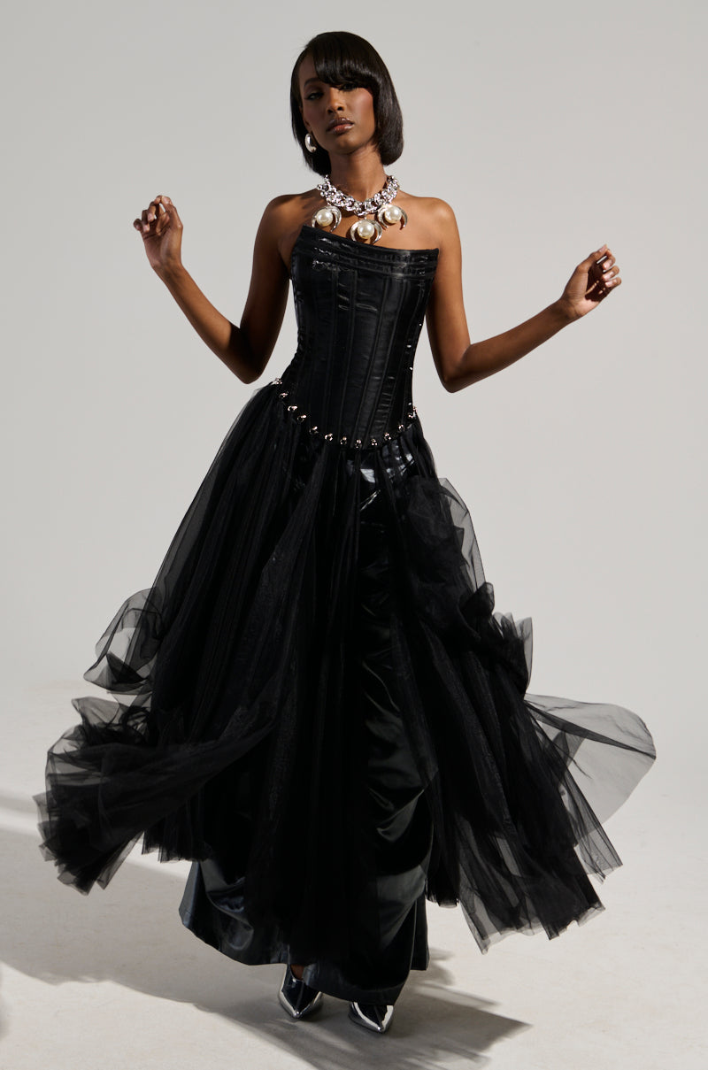 A person poses against a plain background wearing the MARRIED TO THE GAME CORSET TOP IN BLACK, styled as a strapless dress with a satin base and a flowing tulle skirt. They accessorize with a statement necklace and sport short, sleek hair.