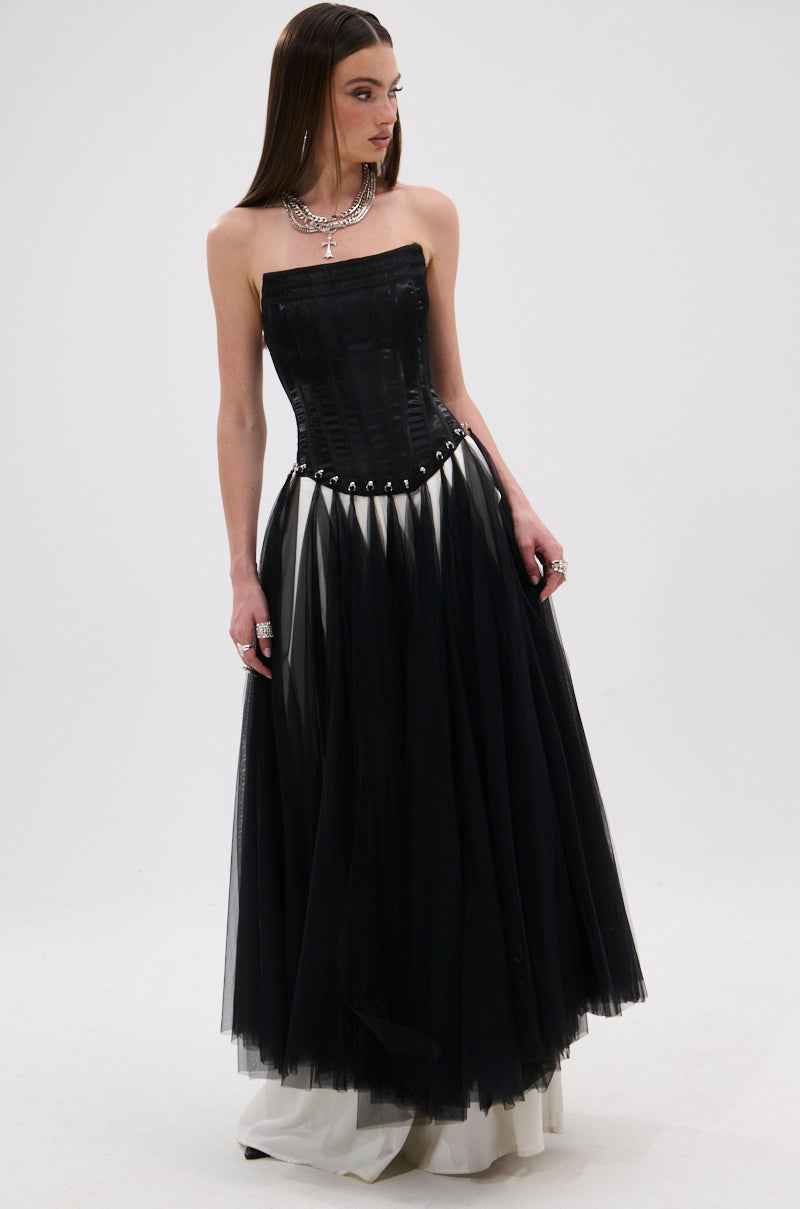 A woman wearing the MARRIED TO THE GAME CORSET TOP IN BLACK, featuring a strapless satin base, lace-up back, and full tulle skirt over a white underskirt, paired with silver jewelry, poses against a plain white background.