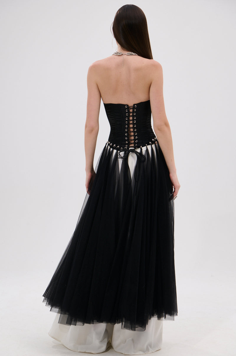 A woman with long straight hair wears the MARRIED TO THE GAME CORSET TOP IN BLACK, featuring a strapless design, lace-up back, and sheer black tulle skirt over a white satin base, against a plain light background.
