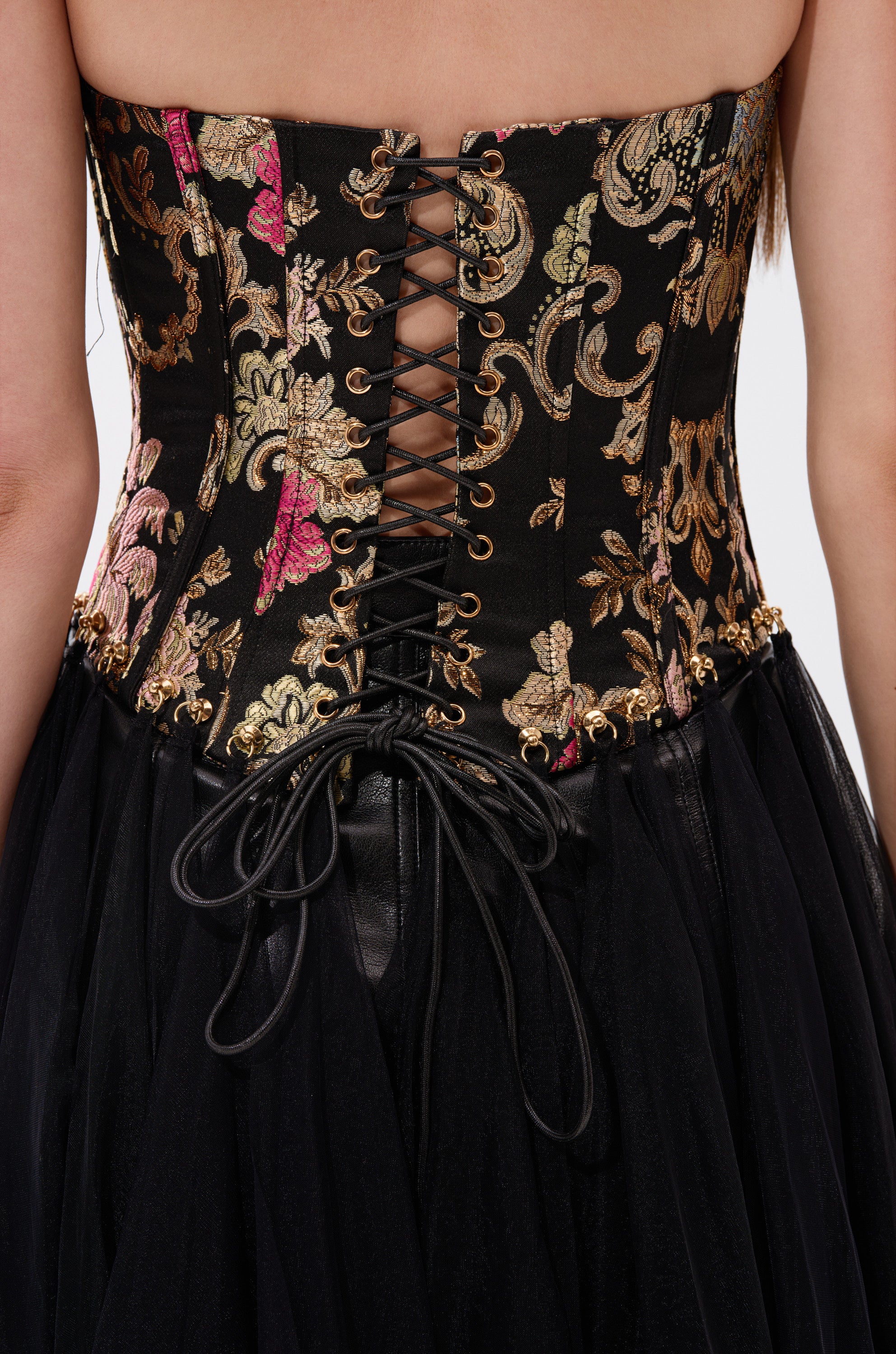 Close-up of a woman's back in the ROYAL TULLE TRIM CORSET TOP, a strapless black corset dress featuring gold and pink floral embroidery, lace-up back, bow waist, and vintage-inspired black tulle skirt. 5