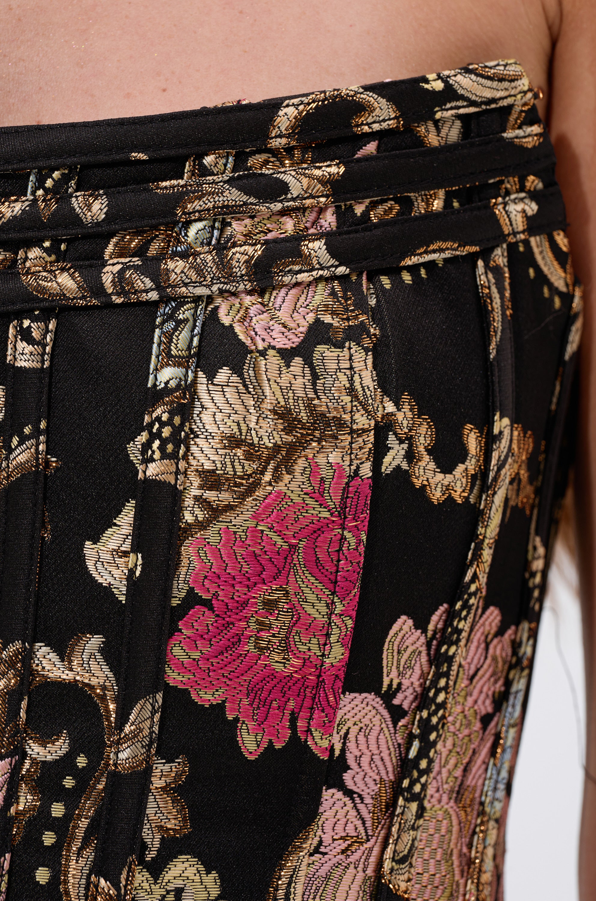 Close-up of the ROYAL TULLE TRIM CORSET TOP, a black fabric piece with ornate gold, pink, and green floral patterns, pleated details, and vintage-inspired stitching, worn by a person. 6