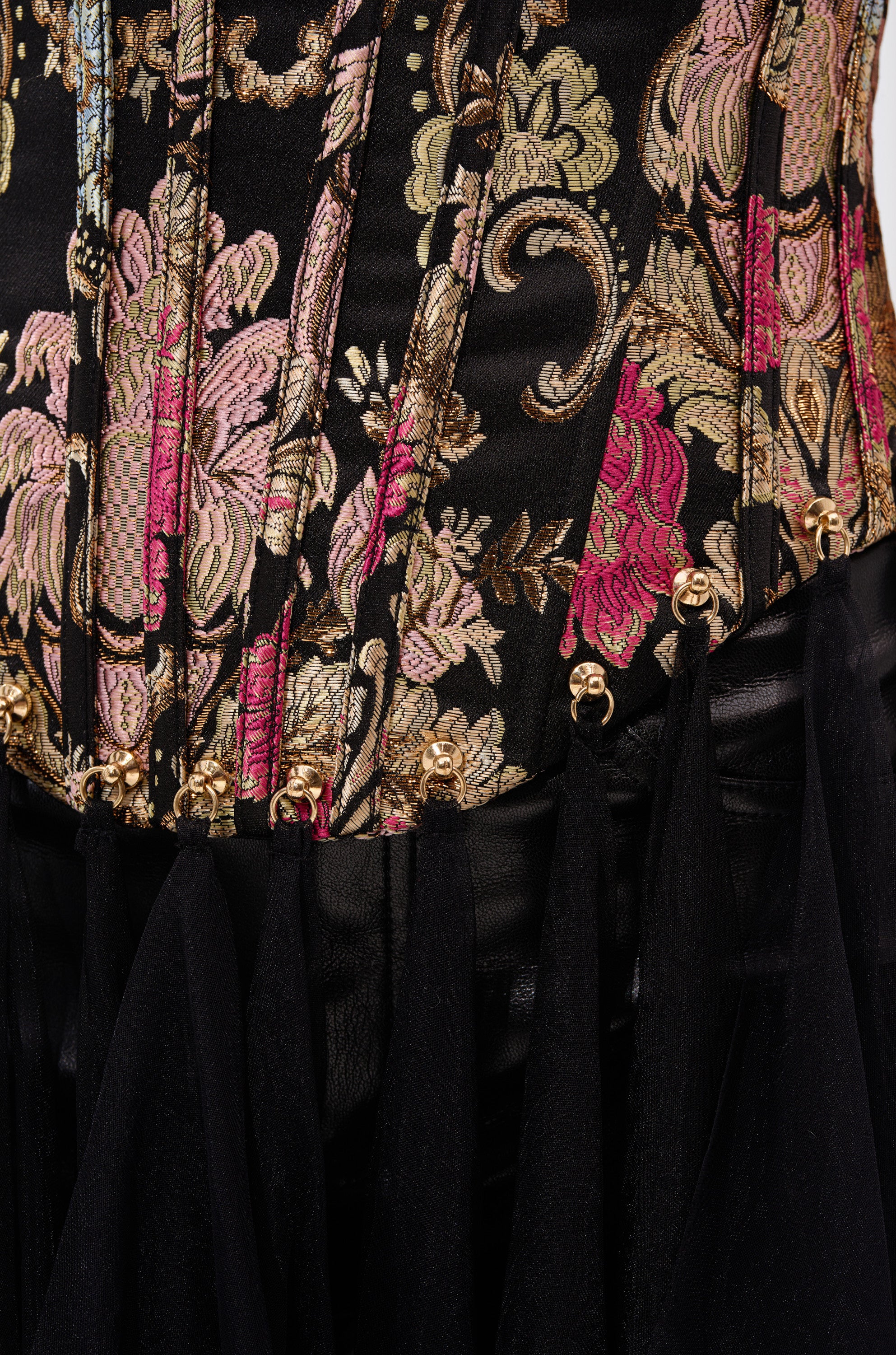 Close-up of the ROYAL TULLE TRIM CORSET TOP: black with pink, gold, and green floral embroidery, vintage-inspired gold embellishments along the bottom edge, and flowing sheer black tulle trim. 7