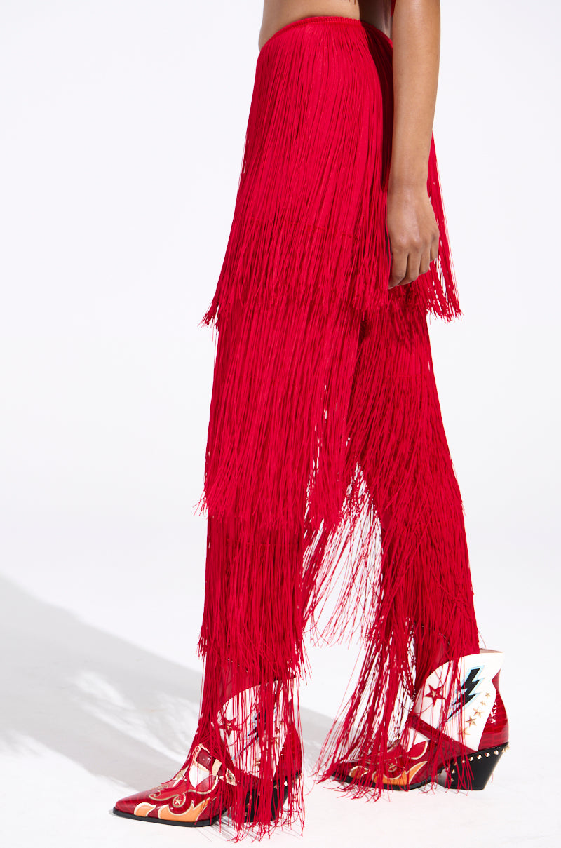 A person is wearing OH SO FRINGE PANTS IN RED, high-rise pants crafted from stretchy fabric, paired with Western-style red and white boots featuring decorative patterns, against a plain white background.