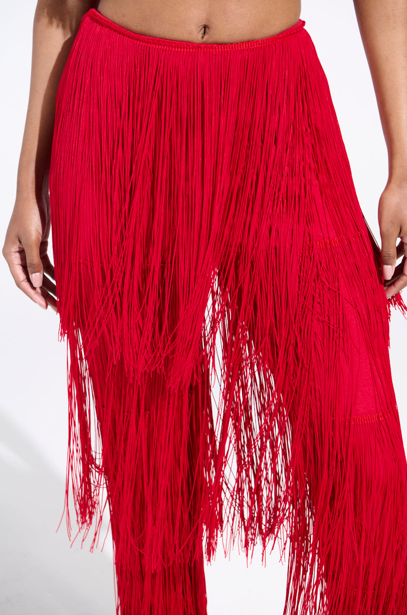 A person showcases the OH SO FRINGE PANTS IN RED, featuring vibrant red color and long, dense fringe that flows elegantly. The stretchy fabric offers comfort and style, set against a plain white background that highlights their bold color and dynamic texture.