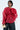 A person poses wearing a sheer red JULIA BUTTON DOWN BLOUSE with ruffled detailing, paired with black pants. They hold a small gold clutch and have hoop earrings, adding elegance with hints of peplum silhouette for flair.