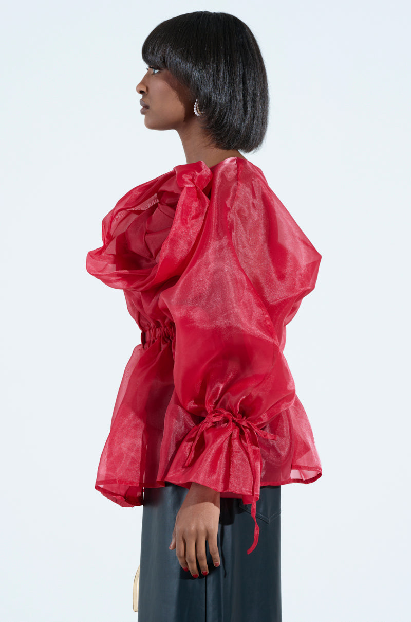 A person with short hair models the JULIA BUTTON DOWN BLOUSE, a puffy, semi-transparent red chiffon top with gathered sleeves and a loose fit. They stand sideways against a plain white background.