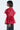 A person with short hair models the JULIA BUTTON DOWN BLOUSE, a puffy, semi-transparent red chiffon top with gathered sleeves and a loose fit. They stand sideways against a plain white background.