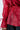 A person models the JULIA BUTTON DOWN BLOUSE, a sheer red chiffon top with button details, elastic waist, and tied cuff sleeves for a subtle peplum effect, styled with dark pants against a plain white backdrop.