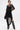 A person stands confidently against a plain white background, wearing the RIPPLING SHEER HALTER TOP over a black outfit with studded knee-high boots, chains, and holding a small black handbag for an avant-garde look.