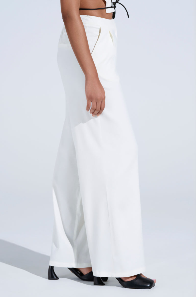 The focus is on the lower half of a person wearing MAYBE NEXT TIME TROUSER, high-waisted white wide-leg pants with abstract embroidery, and black open-toe heeled shoes against a plain background, emphasizing the flowy fabric and style.