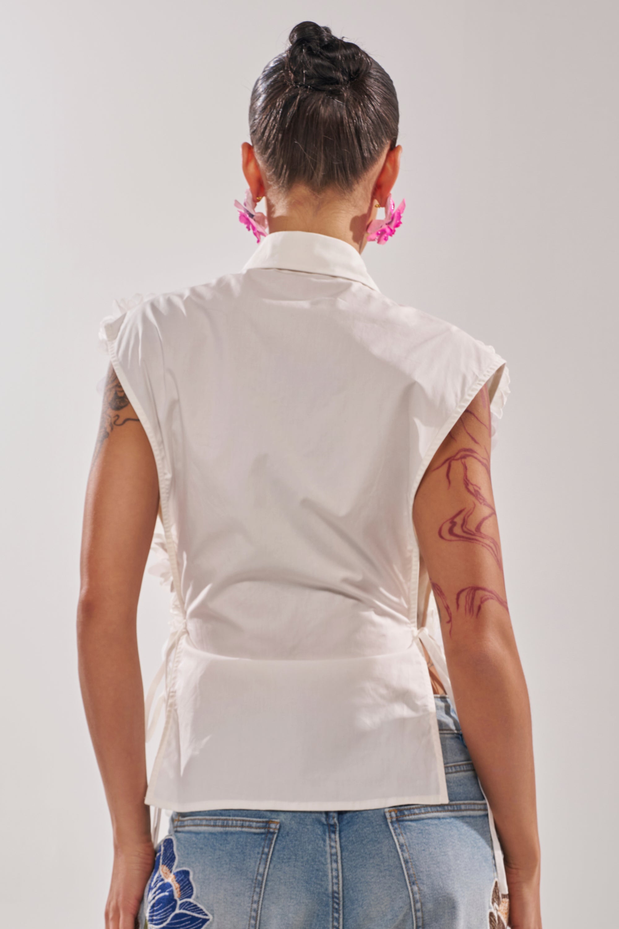 A person with short dark hair is seen from the back, wearing the CRAZY FOR YOU BUTTON DOWN blouse and blue embroidered jeans. They have tattoos on their left arm and large pink earrings. 4