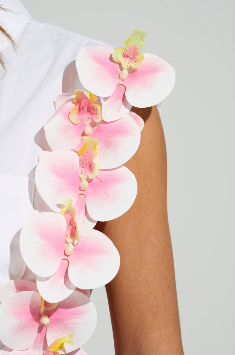 Close-up of a person's arm in the Flower Power Button Down Top, adorned with vertical pink and white orchid appliques with yellow centers and soft pink shading along the shoulder.