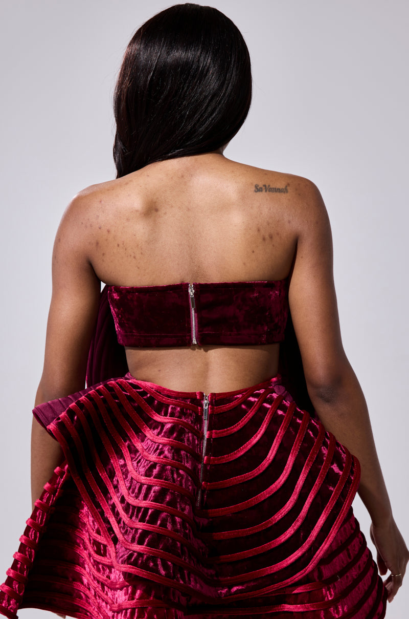 A woman with long dark hair stands with her back to the camera, wearing the STAR OF THE SHOW VELVET BLOUSE and a matching skirt with sheer striped patterns. A small tattoo is visible on her upper right shoulder.