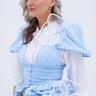 A woman with long gray hair wears a light blue and white striped dress with sheer mesh sleeves and large flower-shaped appliques, styled with the IN BLOOM BROOCH SET. She looks confidently to the side against a plain background.