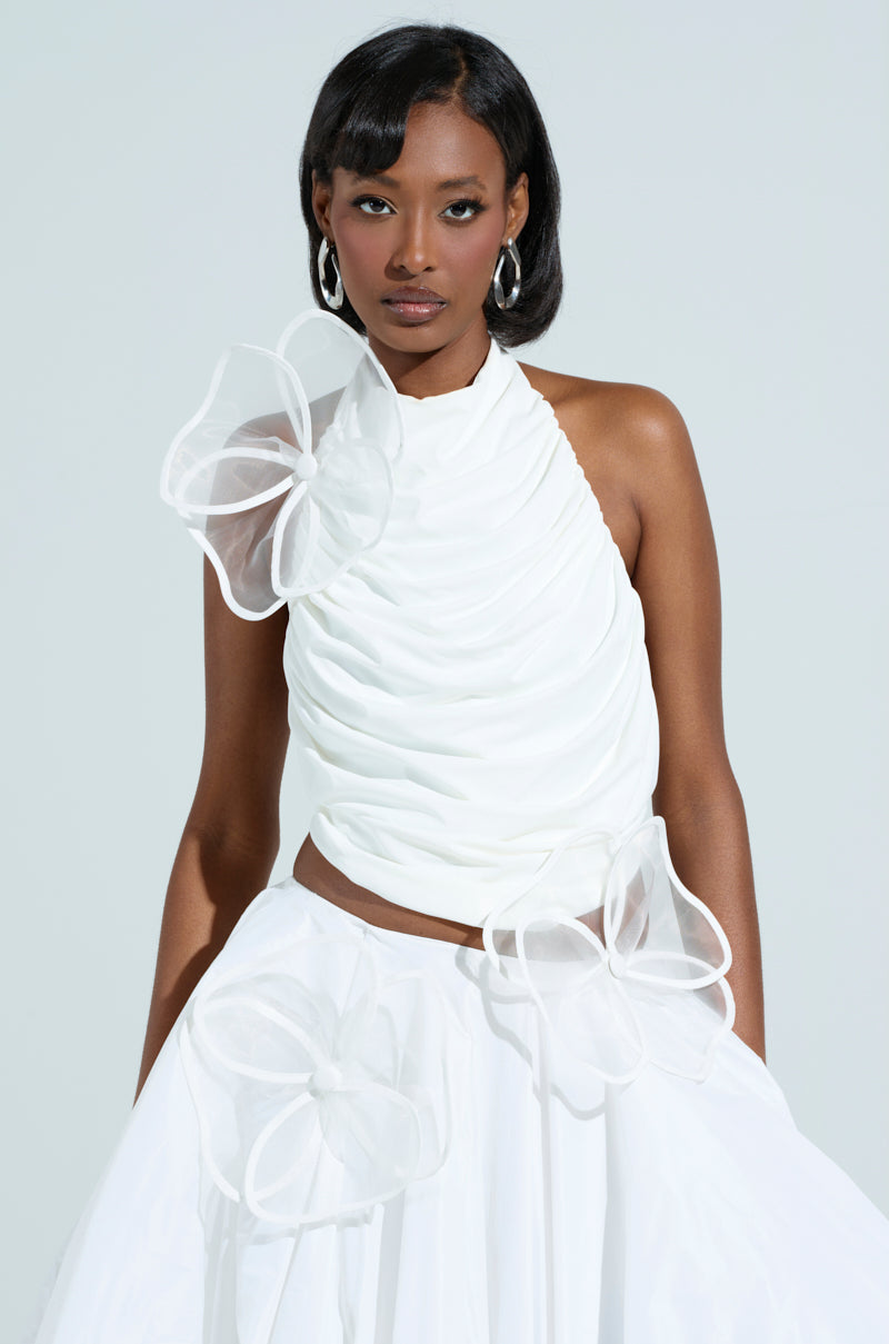 A woman in a chic, sleeveless white dress features flower-shaped appliques from the IN BLOOM BROOCH SET on the shoulder and waist. Her dark hair complements her hoop earrings against a simple, light background. 4