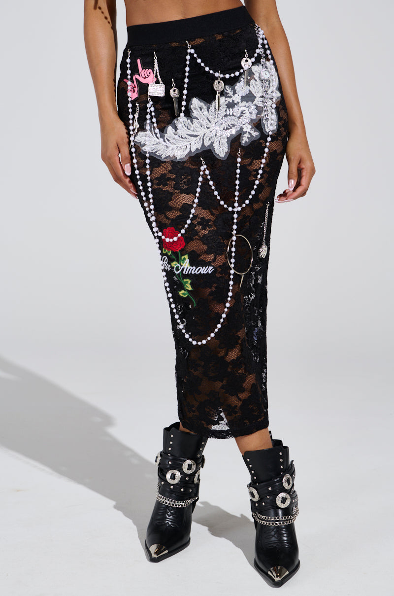 Wearing the CONTROLLED CHAOS LACE MIDI SKIRT with pearl chains, rose appliqué, and white lace details, they pair it with high-rise black boots accented with silver buckles and chains for a chic look that stylishly reveals their midriff.