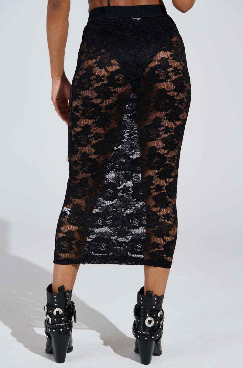 The outfit features a CONTROLLED CHAOS LACE MIDI SKIRT, a stretchy, high-rise black lace piece with a floral pattern that reveals the silhouette, paired with black studded ankle boots with buckles for an edgy yet sophisticated look.