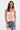 A woman with wavy brown hair models the GOING PLACES CORSET WITH TWEED, a strapless pastel pink bustier top with textured cups, paired with blue jeans featuring lace accents and white text, against a plain white background.