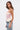 A woman with long brown hair wears the GOING PLACES CORSET WITH TWEED in pastel pink and blue jeans with white lace-up sides, standing against a plain white background.