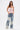 A woman stands confidently in the GOING PLACES CORSET WITH TWEED, a pink and white peplum corset, styled with loose blue jeans detailed with lace panels, clear sections, and 