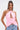 A woman models the FEATHER QUEEN BLOUSE, a sleeveless halter top with pink feather details and a keyhole cutout, paired with light blue jeans. She has long straight hair, colorful earrings, and stands against a plain white background.