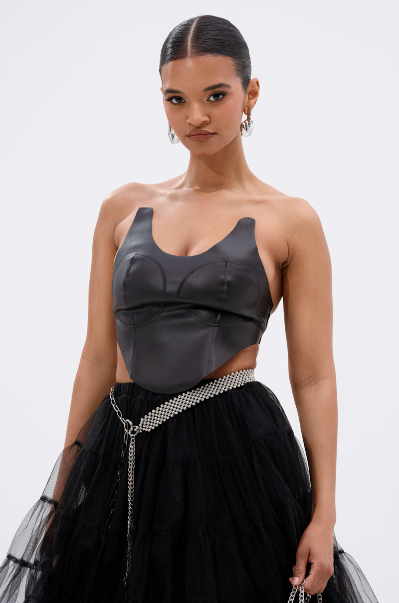 A woman with slicked-back hair wears the SAMMI FAUX LEATHER CORSET and a black tulle skirt with a silver chain belt, posing against a plain white background. 0