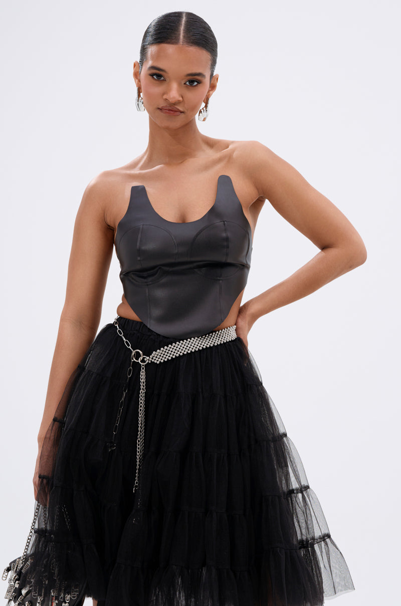 A woman models the SAMMI FAUX LEATHER CORSET with a tiered black tulle skirt, silver chain belt, and hoop earrings. Her hair is sleekly slicked back, all set against a plain background. 1
