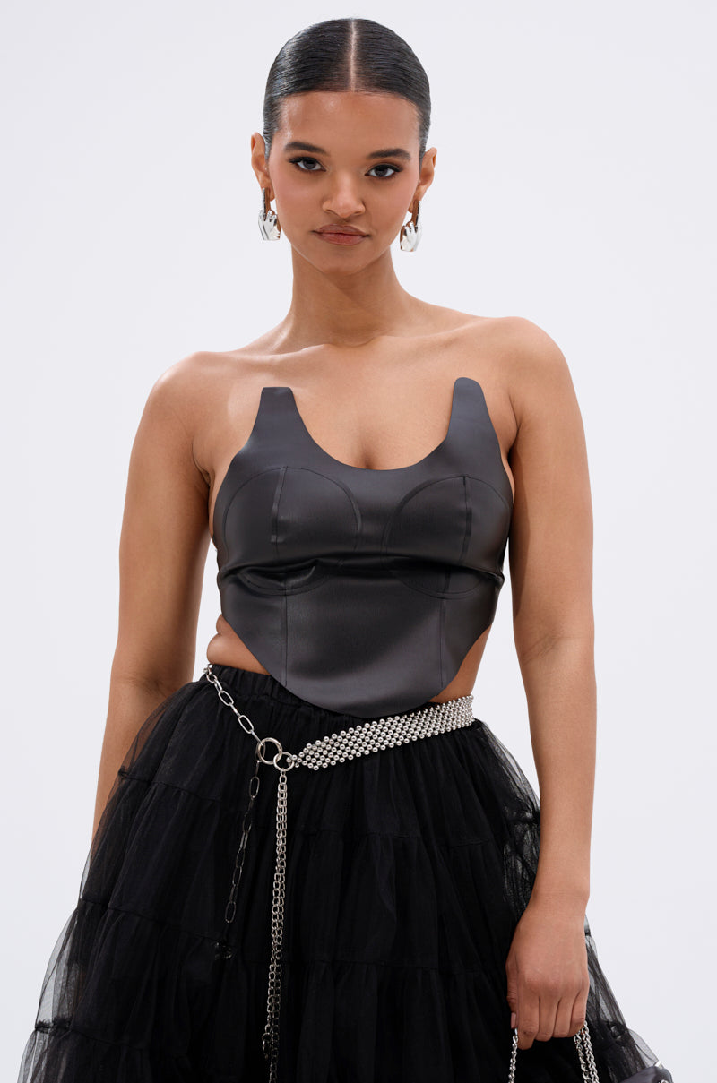 A woman with slicked-back hair models the SAMMI FAUX LEATHER CORSET paired with a layered tulle skirt, hoop earrings, and a chain belt. She stands against a plain white background. 2