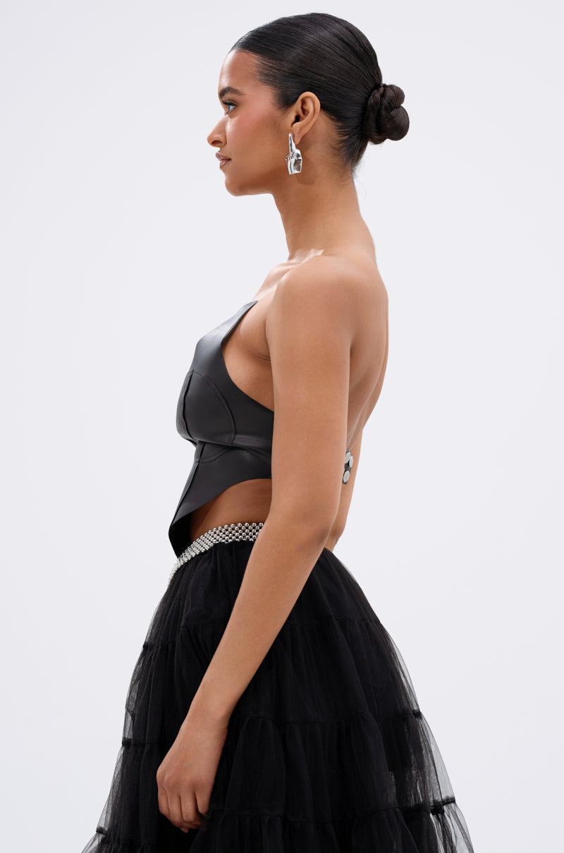 A woman in profile wears the SAMMI FAUX LEATHER CORSET, a tiered black tulle skirt with a jeweled waistband, and silver earrings. Her hair is styled in a sleek bun against a plain light background. 3