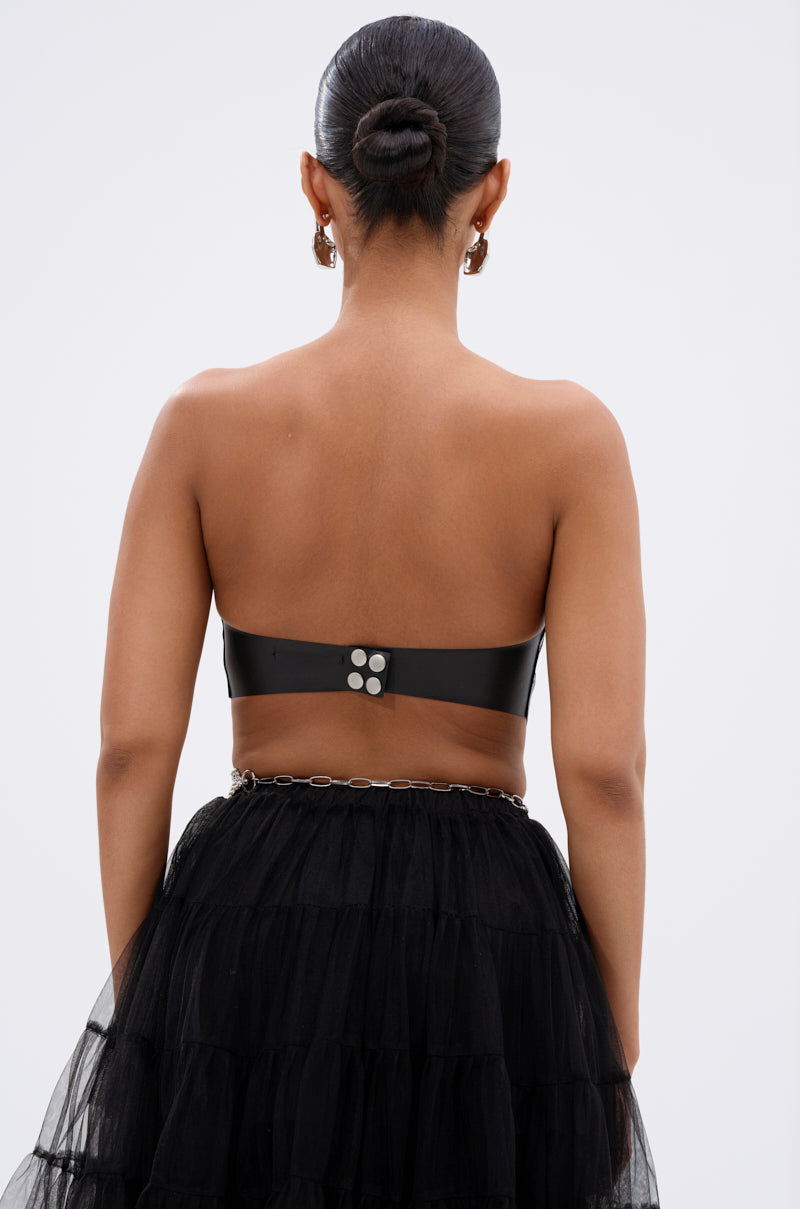 A person with hair in a neat bun is seen from the back, wearing the black SAMMI FAUX LEATHER CORSET with silver buttons and a black tiered tulle skirt with a thin chain belt, set against a plain light background. 4