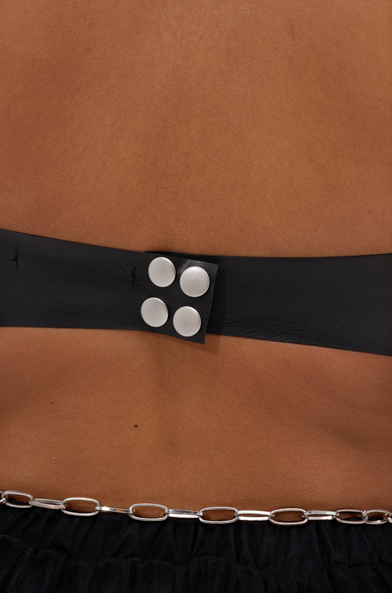 Close-up of a person’s lower back wearing the SAMMI FAUX LEATHER CORSET, featuring black vegan leather with four silver studs and a silver chain detail above black fabric. 7