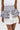 A person wears a white dress with polka dot and striped ruffled peplum corset, finished with the POLKA DOT IT BELT for a playful touch, featuring layered ruffles in both polka dot and striped patterns.