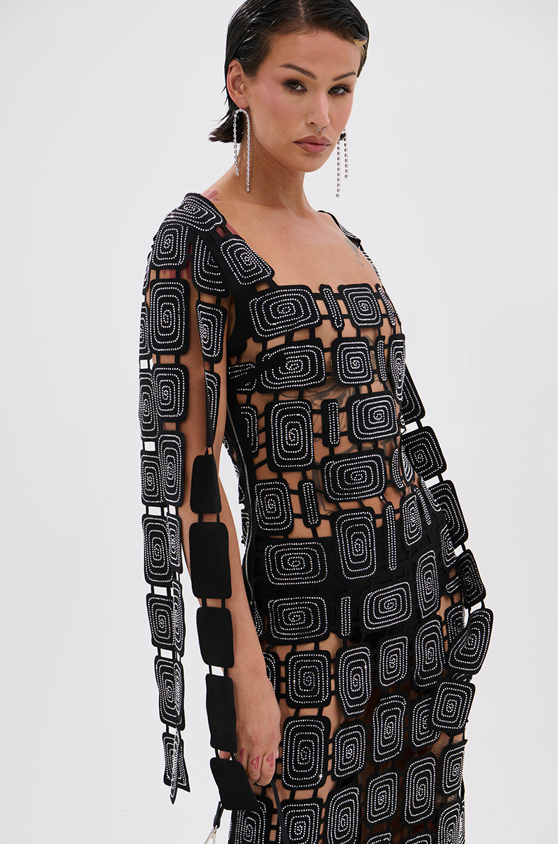 A woman with short dark hair models the ONLY ONE OF ME RHINESTONE MIDI DRESS, showcasing its geometric black and white spiral patterns and rectangular shapes. She completes the look with dangling earrings against a plain white background.