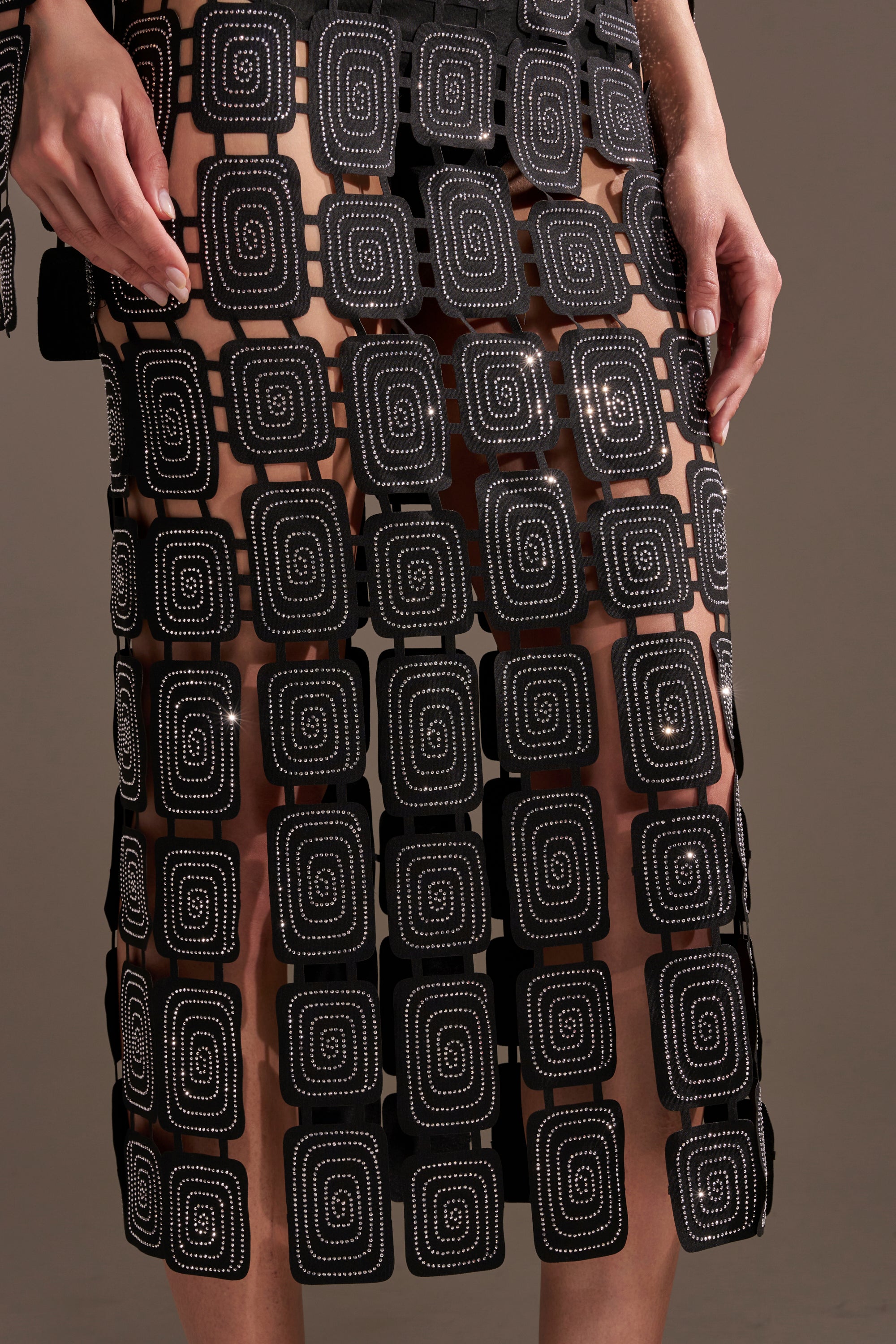 A person wears the ONLY ONE OF ME RHINESTONE MIDI DRESS, a sheer black skirt with white dotted square and spiral grid patterns plus subtle geometric cutouts; their hands rest at their sides against a plain background.