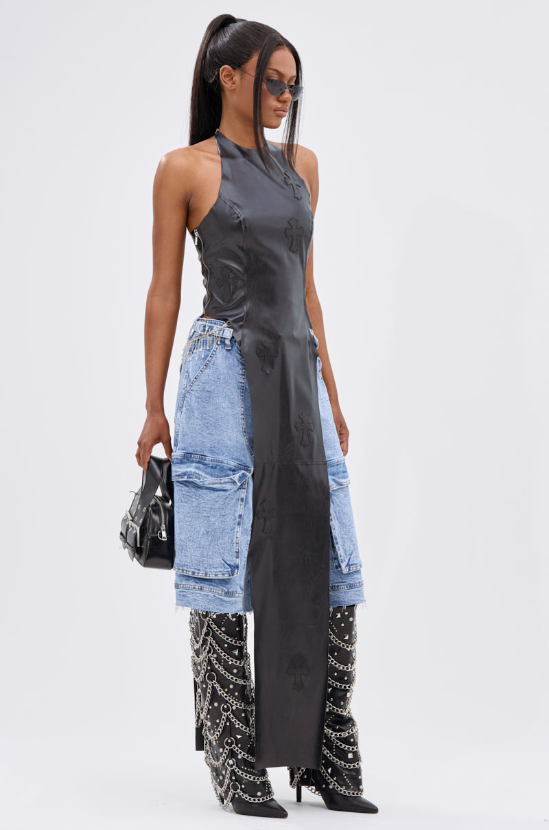 A woman strikes a high-fashion pose against a plain backdrop, wearing sunglasses, the ADDIE FAUX LEATHER BLOUSE, blue cargo denim shorts, black studded knee-high boots, and holding a small black handbag.