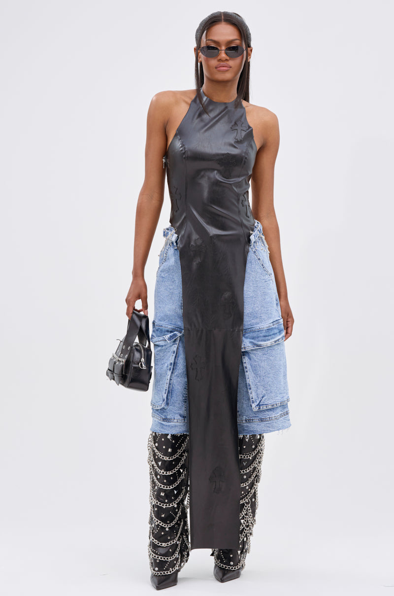 Wearing sunglasses, a black ADDIE FAUX LEATHER BLOUSE, distressed denim shorts, knee-high black boots with chain details, and carrying a small black handbag, a woman strikes an avant-garde pose against a plain white background.
