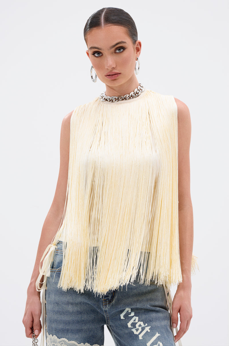 A woman with slicked-back hair wears the SUNSHINE LOVER FRINGE BLOUSE in butter yellow, styled with blue lace-detailed jeans and a chunky silver chain necklace, posing against a white background.