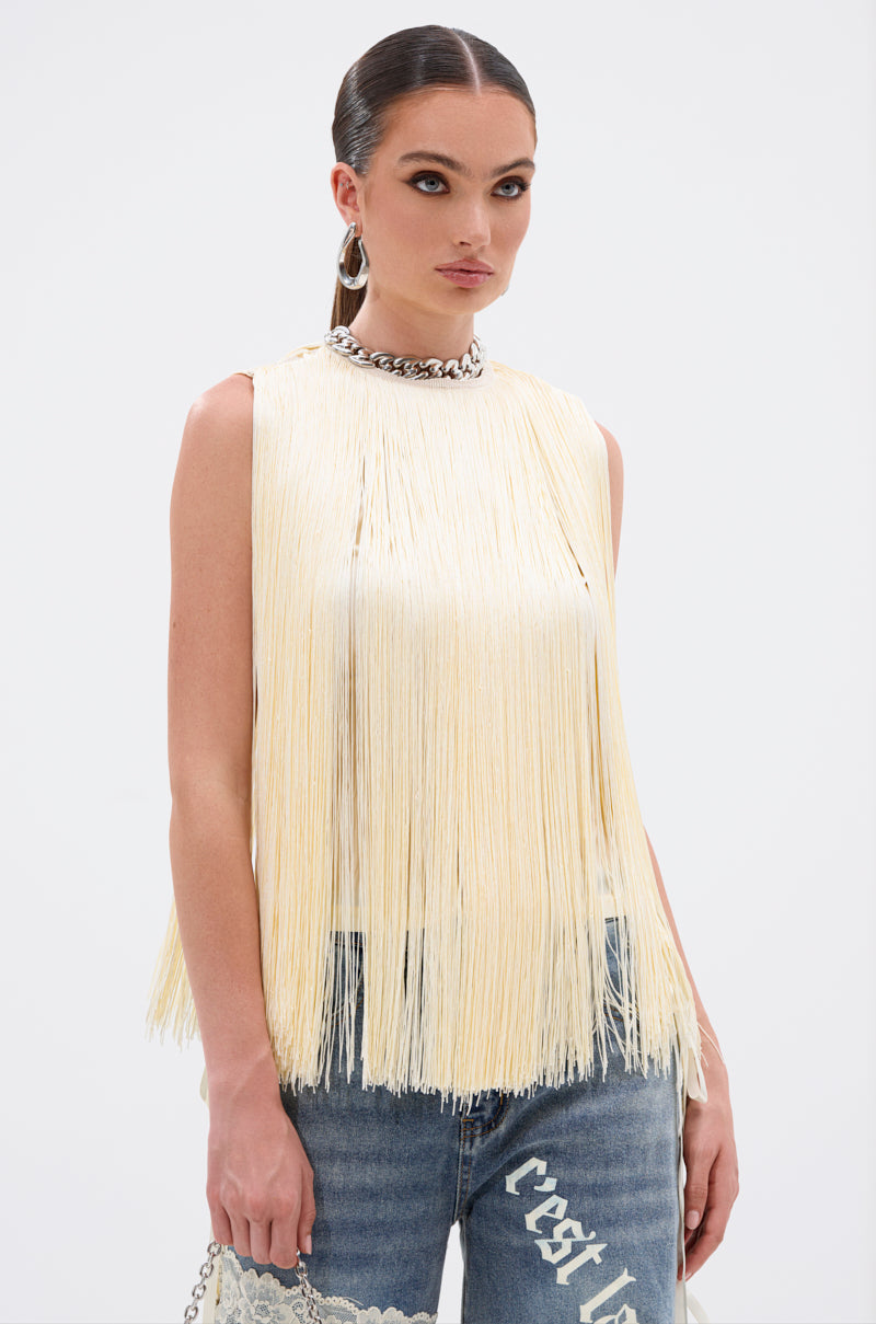 A woman models the SUNSHINE LOVER FRINGE BLOUSE in butter-yellow, styled with a chunky chain necklace, hoop earrings, and light blue jeans with white text—an ideal summer look for trendsetters against a plain white background.